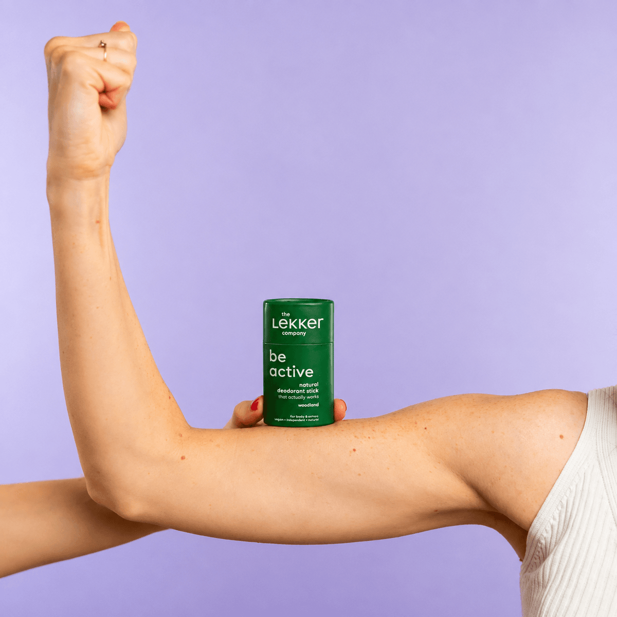 Αποσμητικό stick Be Active της The Lekker Company πάνω σε λυγισμένο χέρι, σε λιλά φόντο.